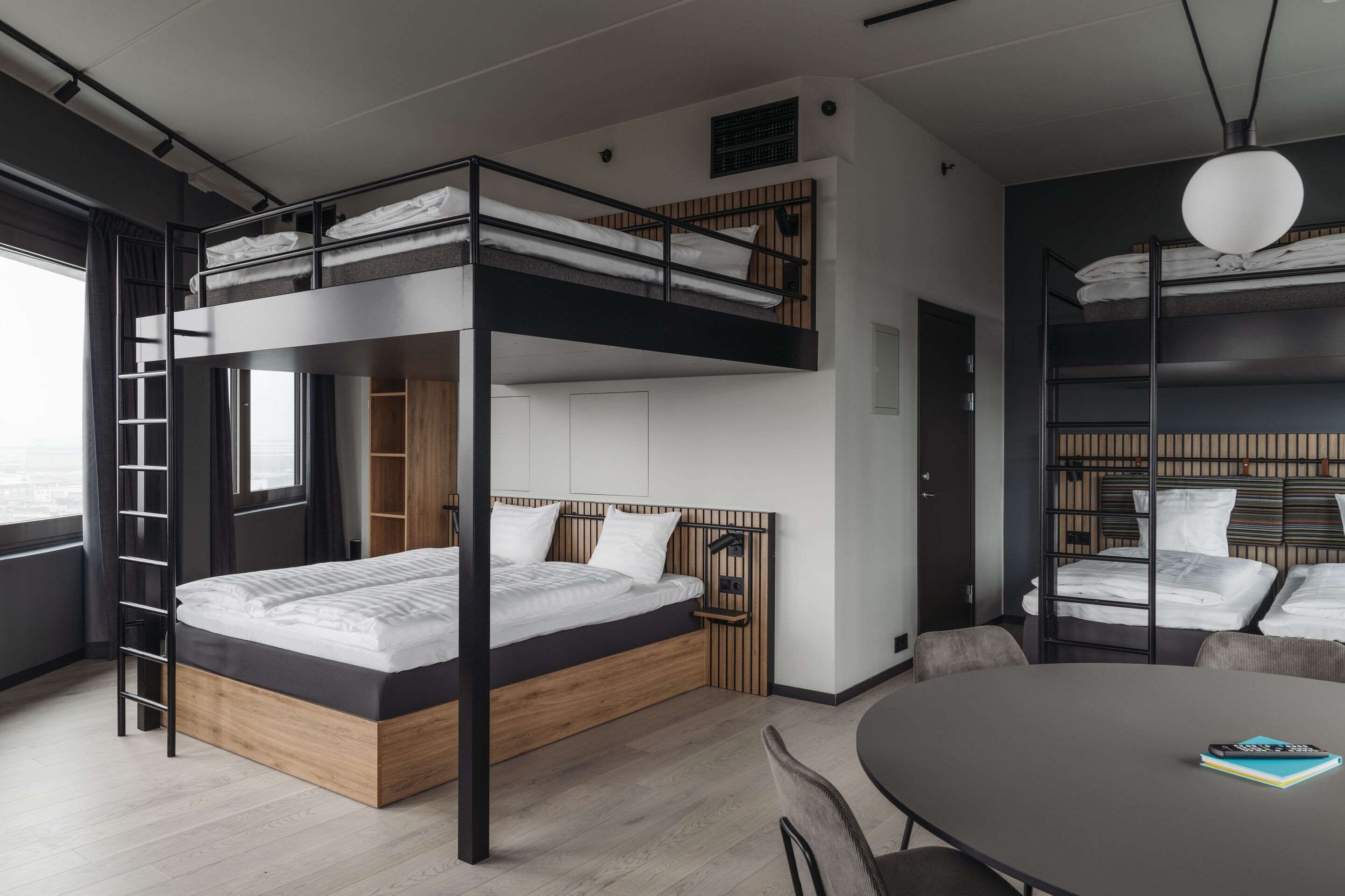 A modern hotel room with a bunk bed, a desk, and a round table.