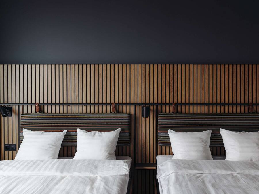 A hotel room with two beds, wooden paneling on the walls, and a striped headboard.