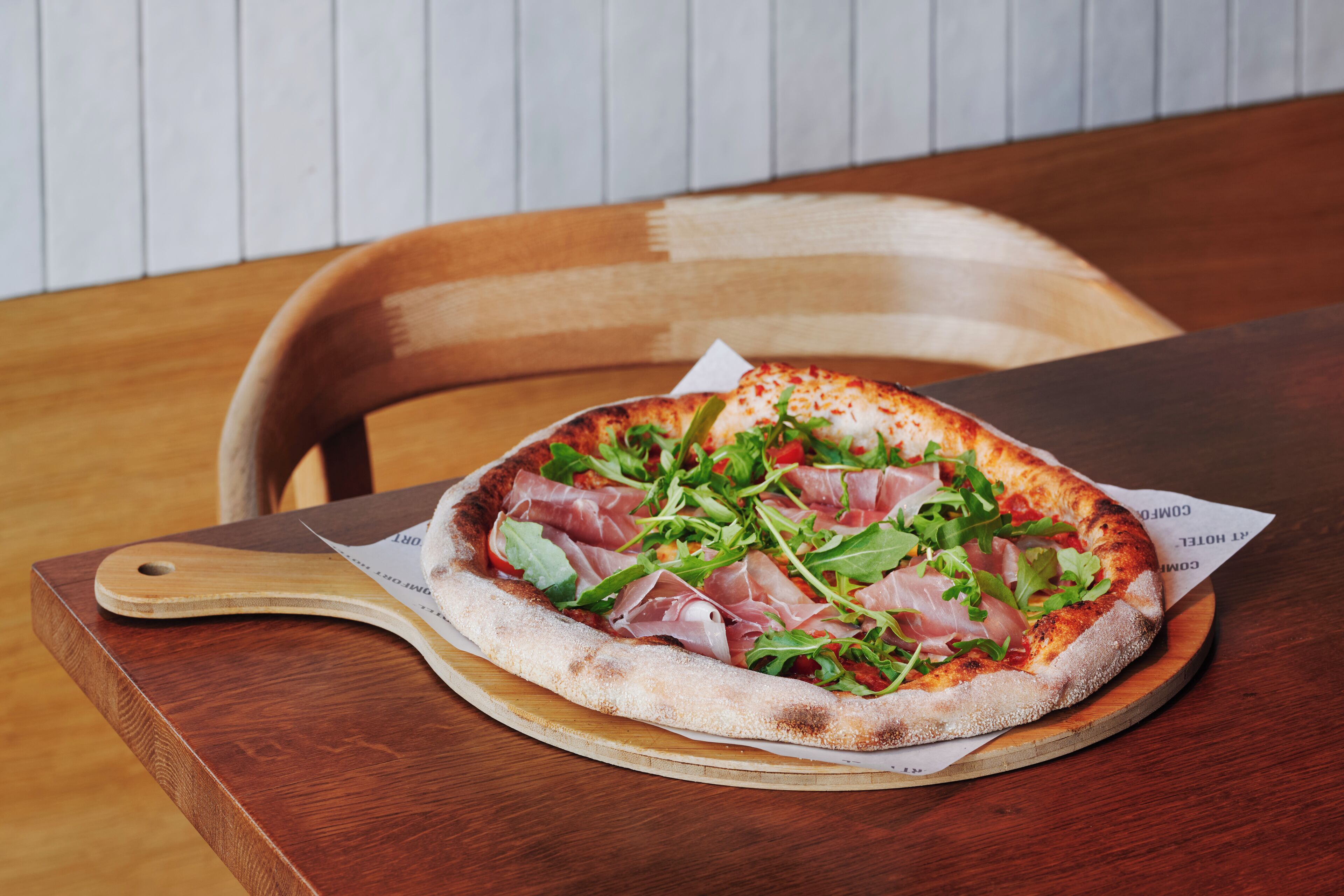 A pizza on a wooden board with a handle, placed on a table.
