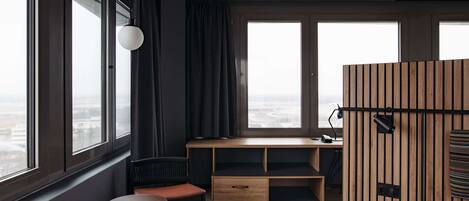 A modern room with a large window, a wooden desk, a bed, and two chairs.