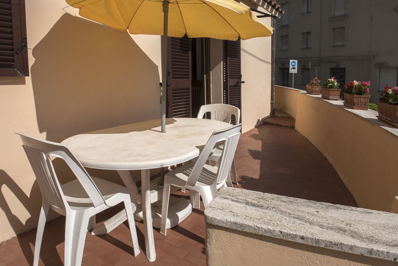 Un balcon avec une table ronde et des chaises, un parasol jaune et des plantes en pot.