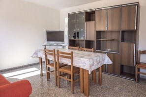 A dining area with a table and chairs, a television, and a large wooden cabinet with shelves.