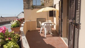 Ein Balkon mit Tisch und Stühlen, Blumentöpfen und einer Tür mit Fensterläden.
