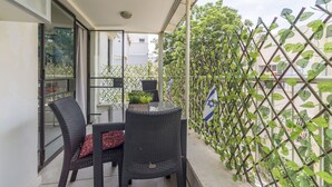 A balcony with wicker chairs, a glass table, and a view of a cityscape. - Gordon Beach Ruppin street Best location (Tel Aviv-Yafo)
