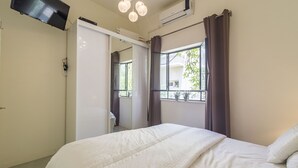A bedroom with a bed, a TV mounted on the wall, an air conditioning unit, and a window with curtains. - Gordon Beach Ruppin street Best location (Tel Aviv-Yafo)