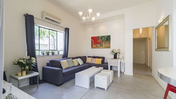 A modern living room with a dark blue sofa, white coffee table, and a painting on the wall. - Gordon Beach Ruppin street Best location (Tel Aviv-Yafo)