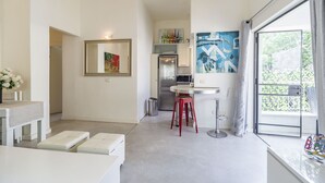A modern kitchen with a refrigerator, a dining area with a white table and red stools, and a large window with a view of greenery. - Gordon Beach Ruppin street Best location (Tel Aviv-Yafo)
