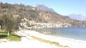 A beach with a clear view of a mountain range in the background, a path leading to the beach, and a green trash bin.