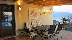 A terrace with a table and chairs, a chandelier, and a painting on the wall.