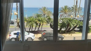 Quarto com uma grande janela que dá para a rua, com carros estacionados e palmeiras.