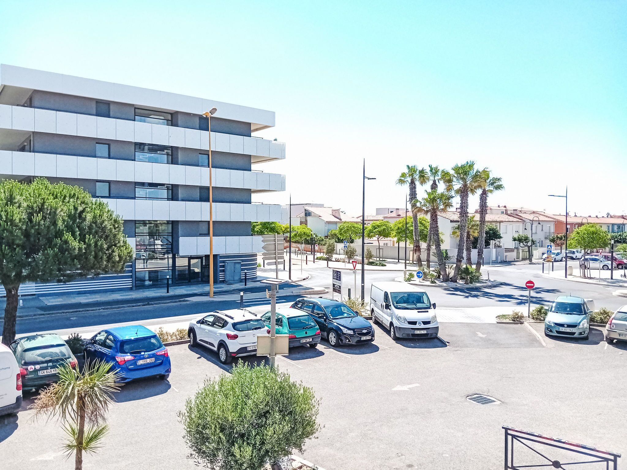 A parking lot with multiple cars and a modern building with a flat roof and large windows.
