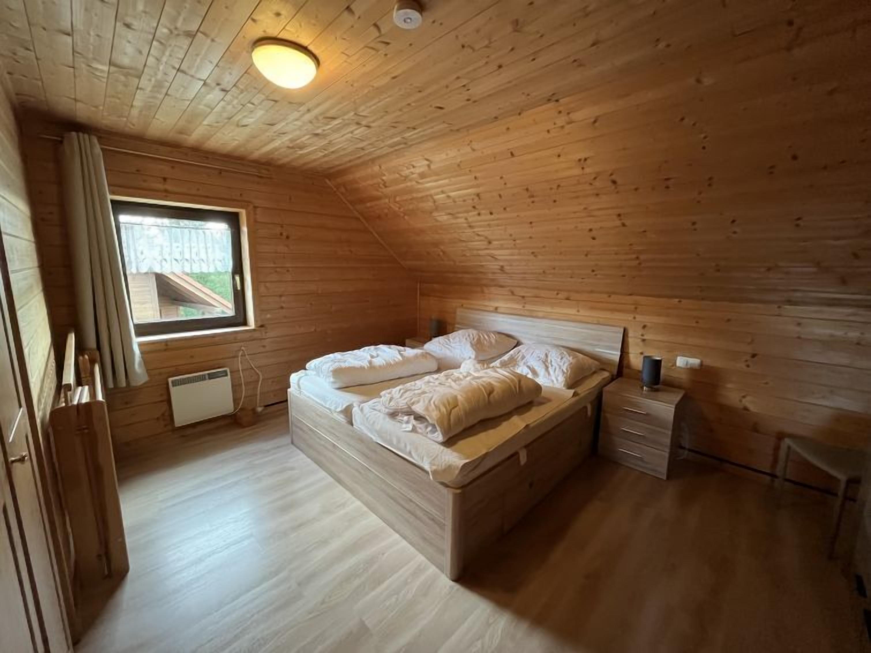 A wooden cabin bedroom with a bed, a nightstand, a window, and a ceiling light.
