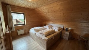 Un dormitorio de cabaña de madera con cama, mesita de noche, ventana y luz de techo.