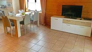 Un comedor con una mesa y sillas, un televisor sobre un mueble, y una ventana con cortinas.