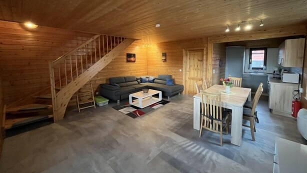 Un interior de madera con una escalera, un sofá, una mesa de comedor y una zona de cocina.