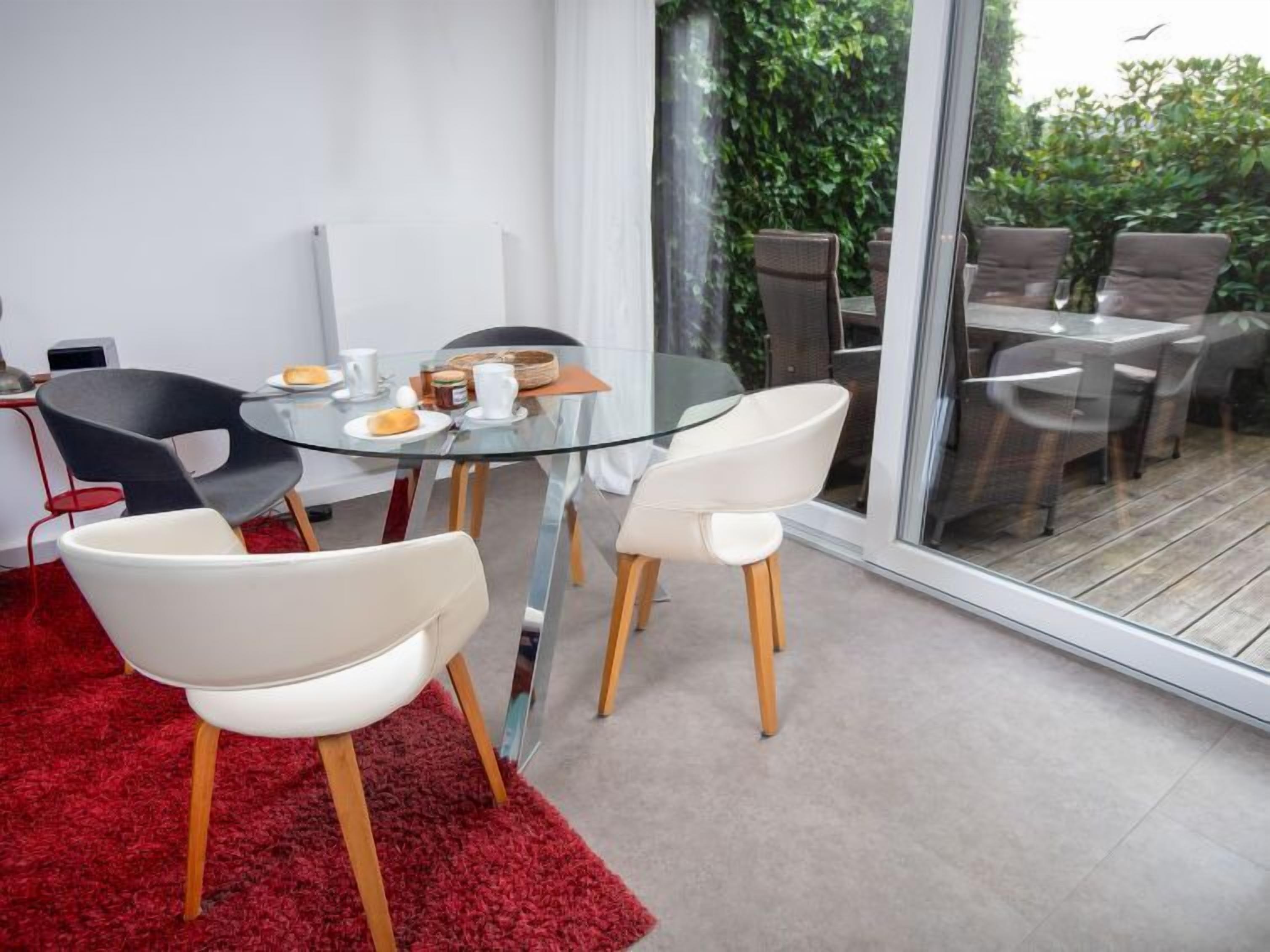 Un espace repas moderne avec une table en verre, des chaises blanches et noires, et un tapis rouge.