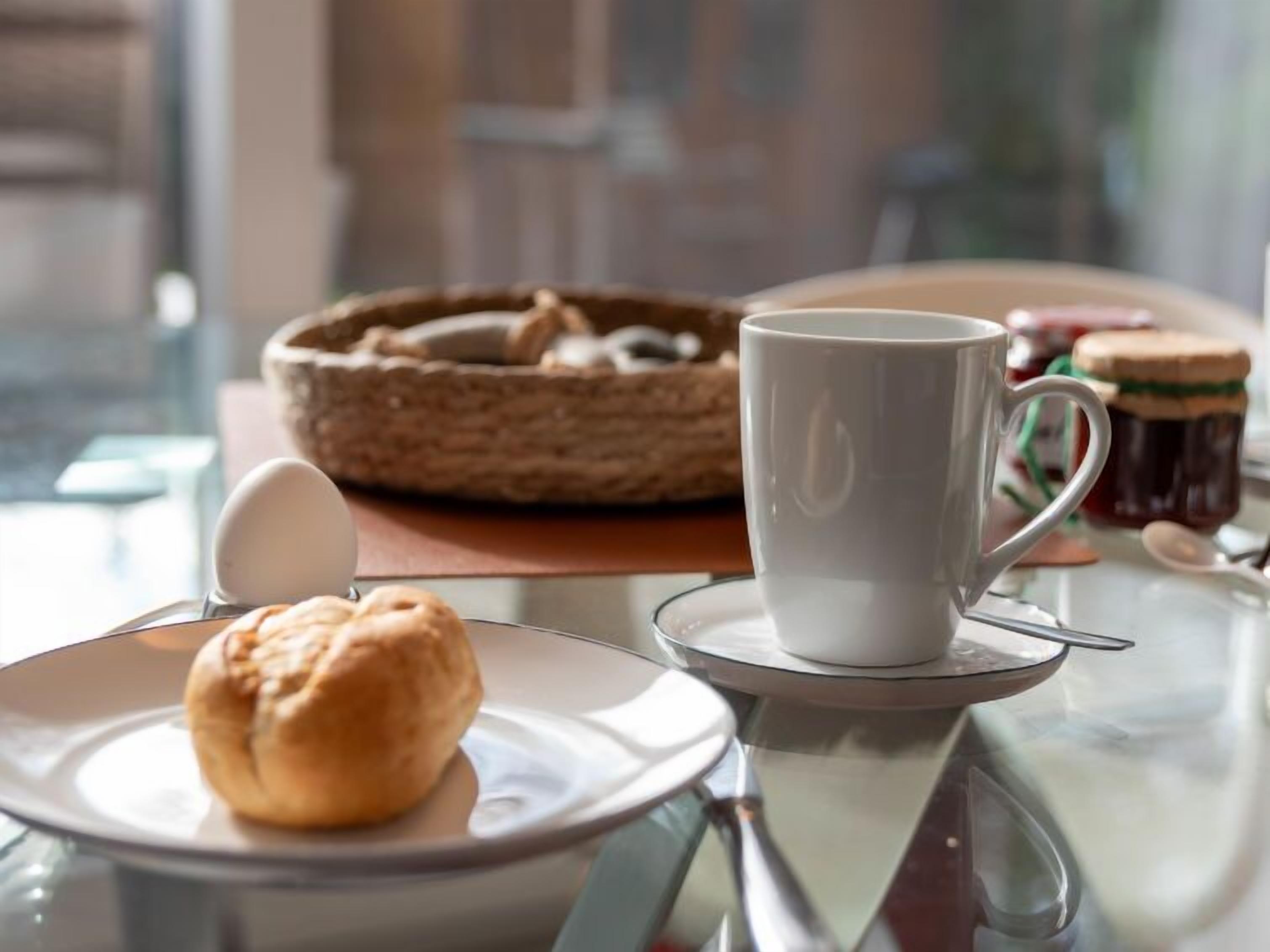 Une table mise pour le petit-déjeuner, avec une assiette de viennoiseries, une tasse de café et un pot de confiture.