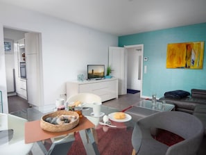 Ein modernes Wohnzimmer mit einem Glastisch, einer Couch und einem Fernseher auf einem weißen Schrank.