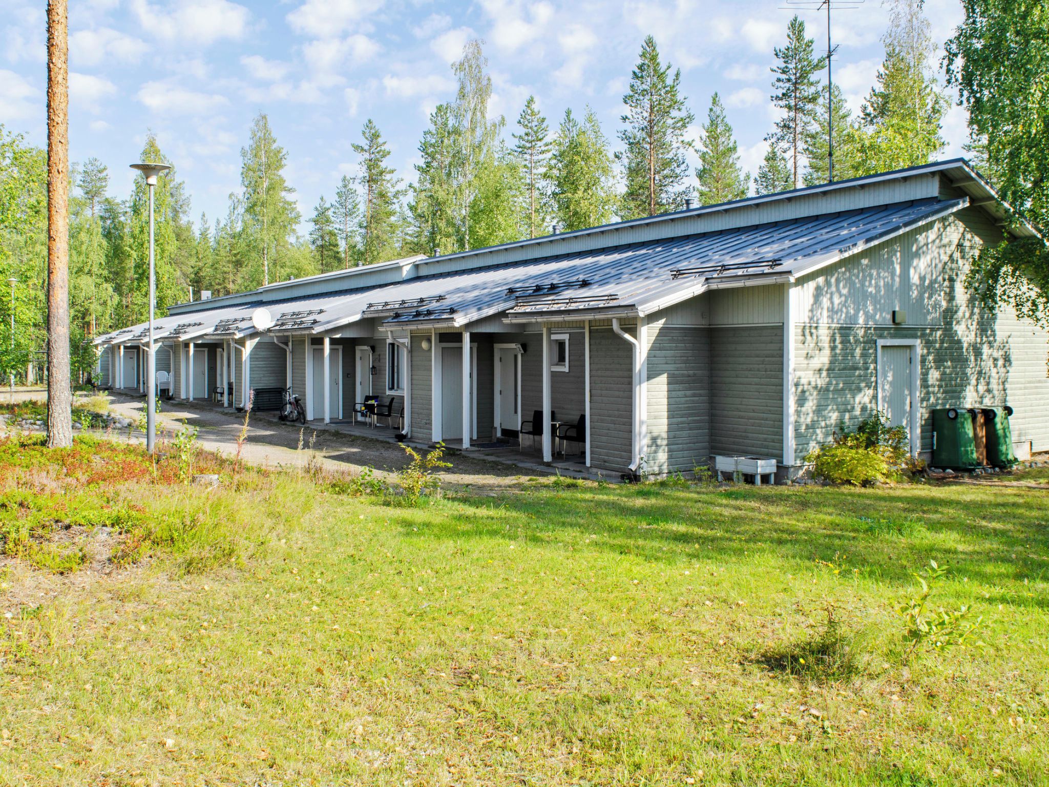 Une rangée de chalets de plain-pied, chacun doté d’une véranda, entourés d’une pelouse et d’arbres.