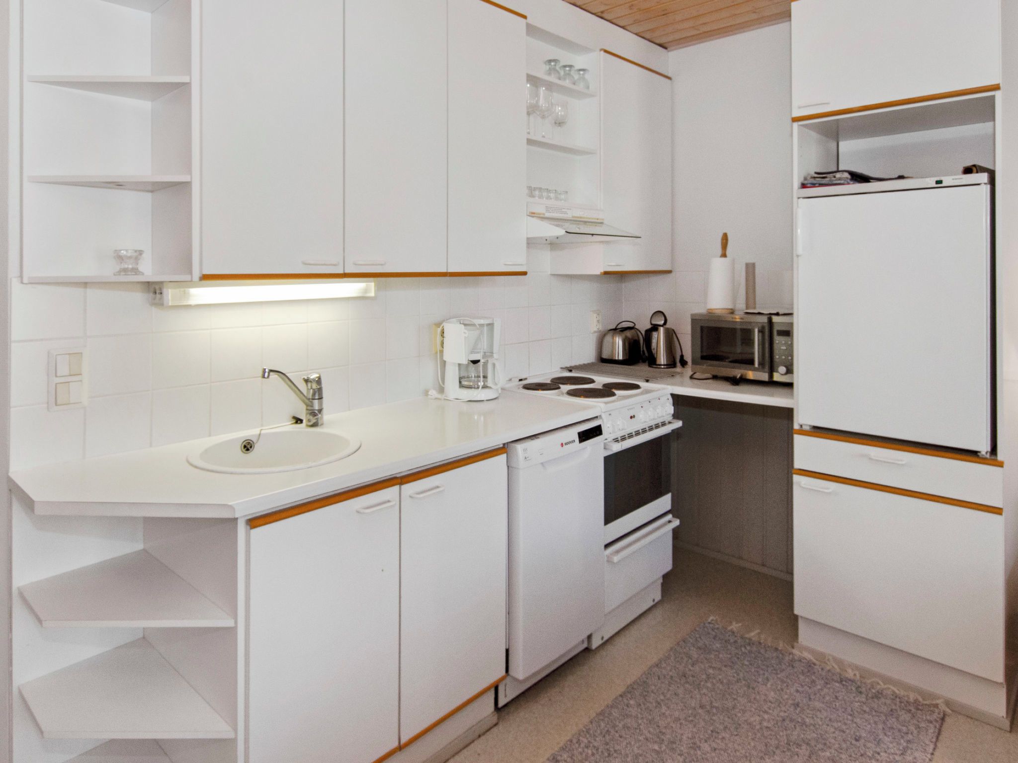 Une cuisine moderne avec des meubles blancs, un évier, une cuisinière, un four à micro-ondes et une machine à café.