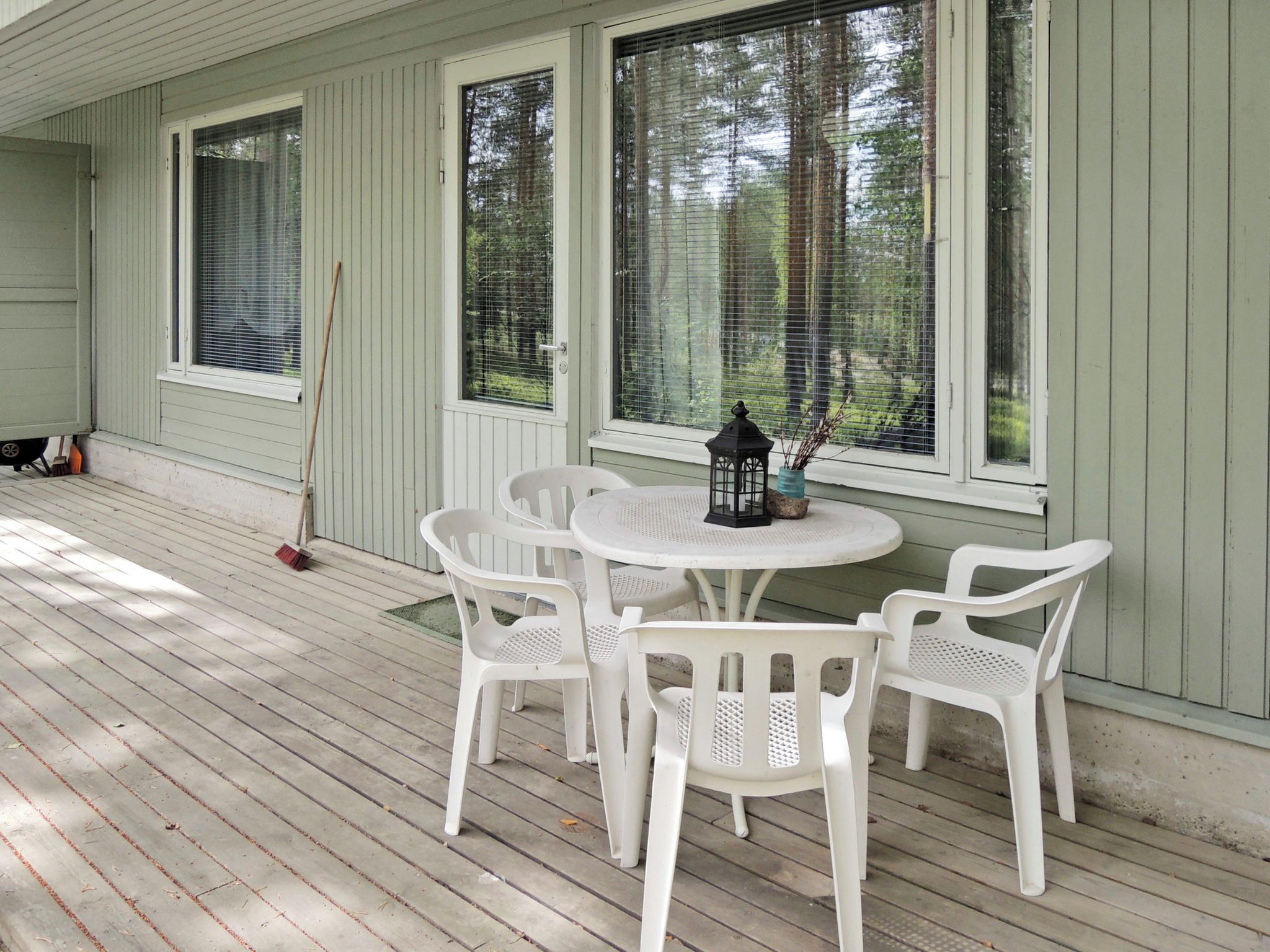 A covered porch with a round table and four chairs, a broom, and a lantern.