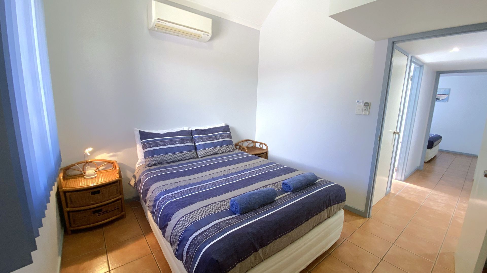 Ein Schlafzimmer mit einem Bett, Nachttischen, einer Wand-Klimaanlage und einer Tür zu einem anderen Raum.