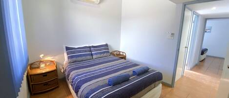 Ein Schlafzimmer mit einem Bett, Nachttischen, einer Wand-Klimaanlage und einer Tür zu einem anderen Raum.
