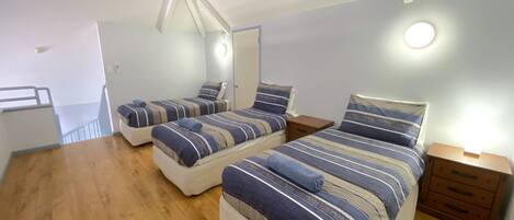 A bedroom with two beds, wooden flooring, and a small bedside table with a lamp.