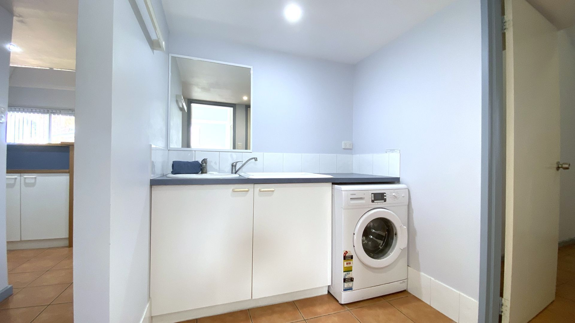 Une petite buanderie moderne, équipée d’un lave-linge, d’un évier et d’un miroir.