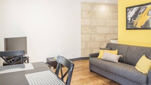 A living room with a gray sofa, a TV, a table with a keyboard, and a stone wall.