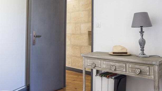 A room with a grey door, a wooden desk with a lamp, and a hat on the desk.