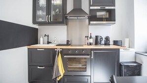 A modern kitchen with dark cabinetry, a stainless steel range hood, a built-in oven, and a coffee maker.