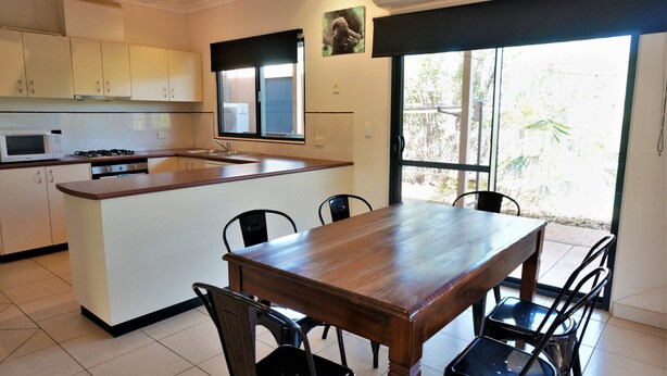 Una cocina compacta con una isla central, una mesa de comedor con sillas y un amplio ventanal que proporciona luz natural.