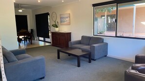 Sala de estar con un sofá gris, una mesa de centro y un aparador de madera. Se ve una ventana con vistas al exterior.