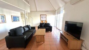 Ein modernes Wohnzimmer mit zwei schwarzen Sofas, einem Holztisch und einem Fernseher auf einem Holzständer.