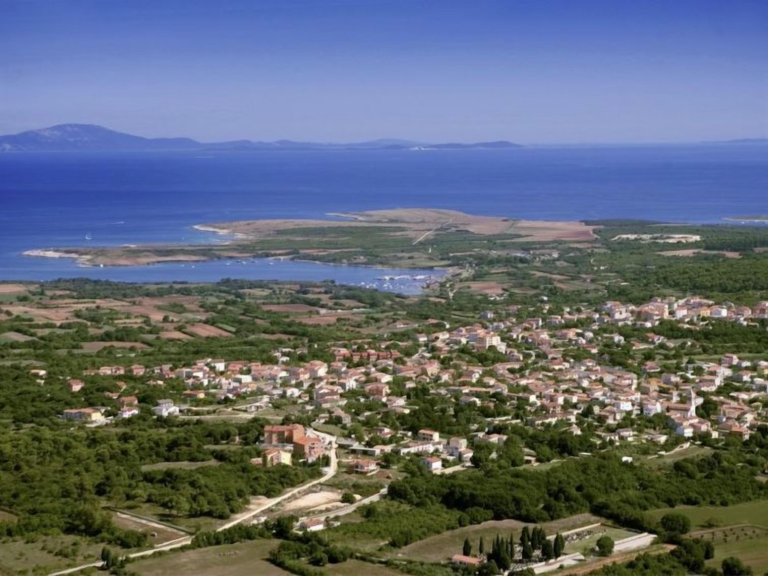 An aerial view of a coastal town with a dense cluster of houses, a marina, and a large body of water.