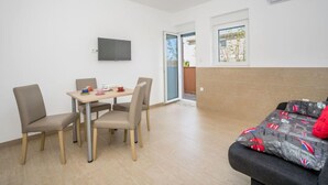 A room with a bed, a TV mounted on the wall, a table with chairs, and a window.