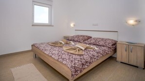 A bedroom with a bed, a nightstand, a window, and a wall-mounted light fixture.