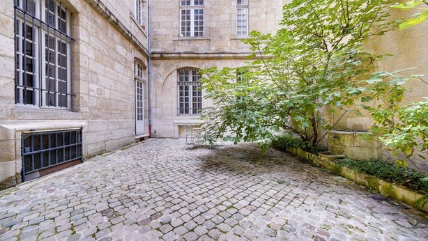 A courtyard with cobblestone flooring, stone walls, and a tree. - Leyteire large one bedroom apartment (BORDEAUX)