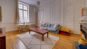A living room with a wooden coffee table, a grey sofa, and a dining area with a table and chairs. - Leyteire large one bedroom apartment (BORDEAUX)