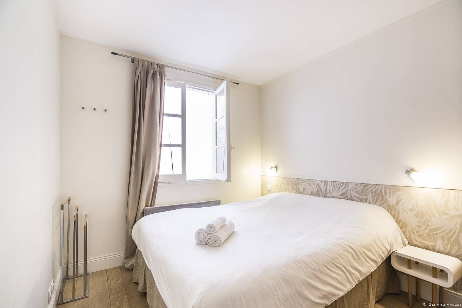 Habitación de hotel con una cama grande, una mesita de noche, una ventana con cortinas y un cabecero con lámpara.