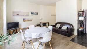 A living room with a TV, a sofa, a dining table with chairs, and artwork on the walls. - Bright and comfortable apartment - 2nd FLOOR (BORDEAUX)