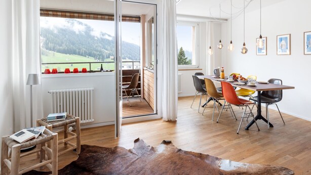 Ein moderner Essbereich mit Holztisch, Stühlen und Blick auf die Berge durch große Fenster.