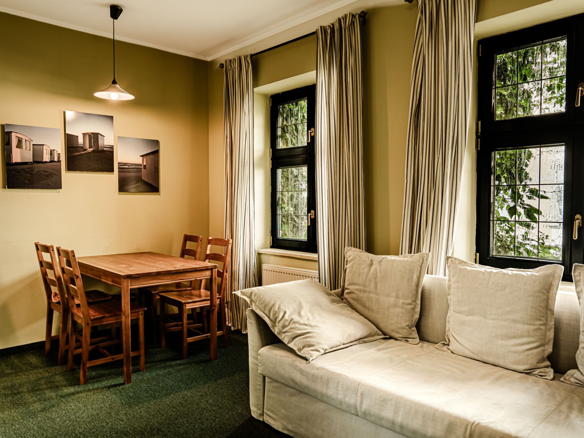 Una habitación acogedora con una mesa de comedor de madera, cuatro sillas, un sofá color beige con cojines y una ventana con cortinas.