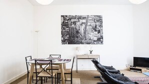 A modern living room with a dining table, chairs, a sofa, a TV, and a cityscape artwork on the wall. - Martinique Street (BORDEAUX)