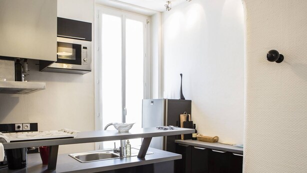 A compact kitchen with a built-in microwave, a small sink, and a window providing natural light. - Martinique Street (BORDEAUX)