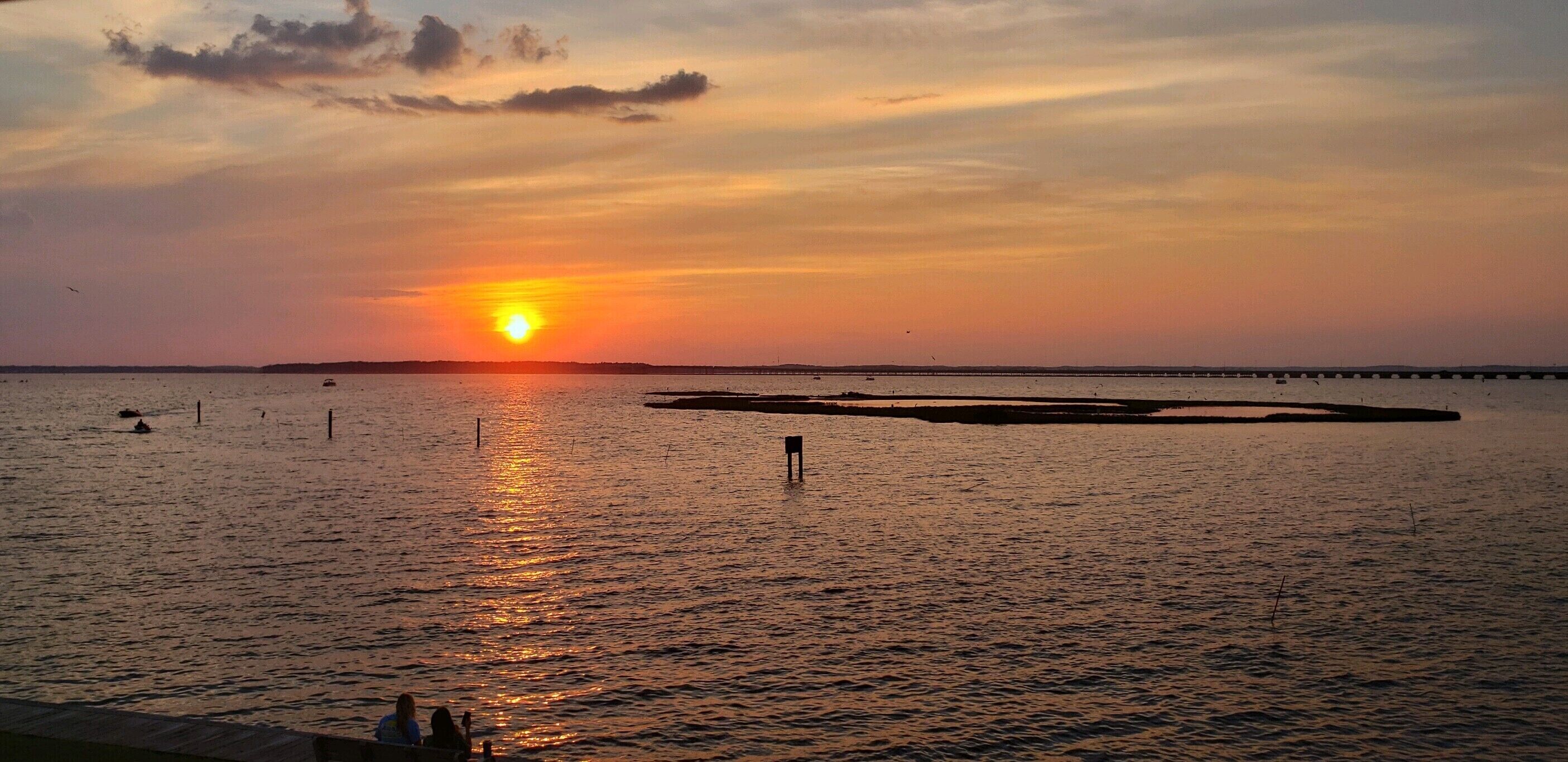 A sunset over a calm body of water with a pier extending into the water.