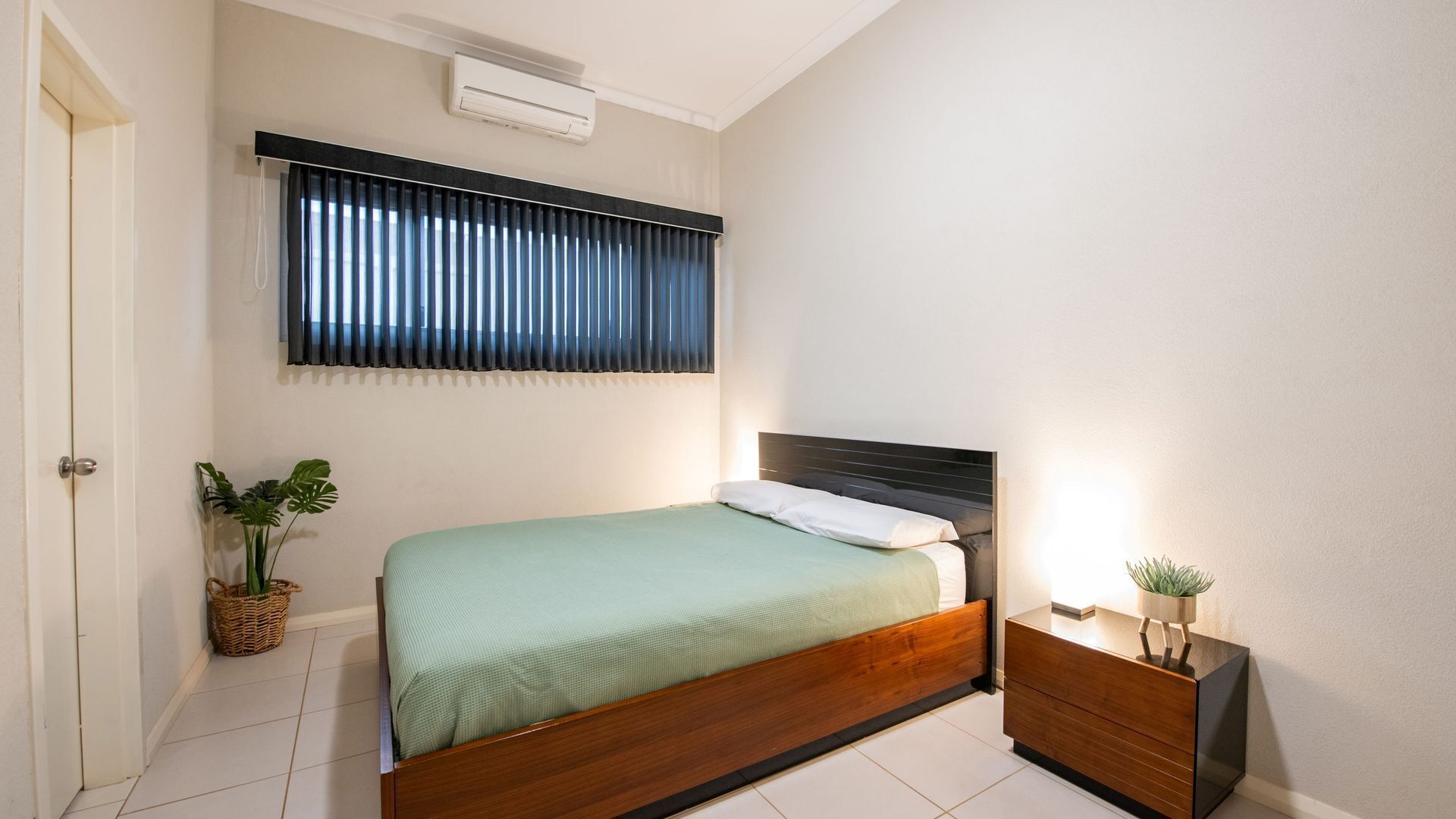A bedroom with a bed, bedside table, and a potted plant.
