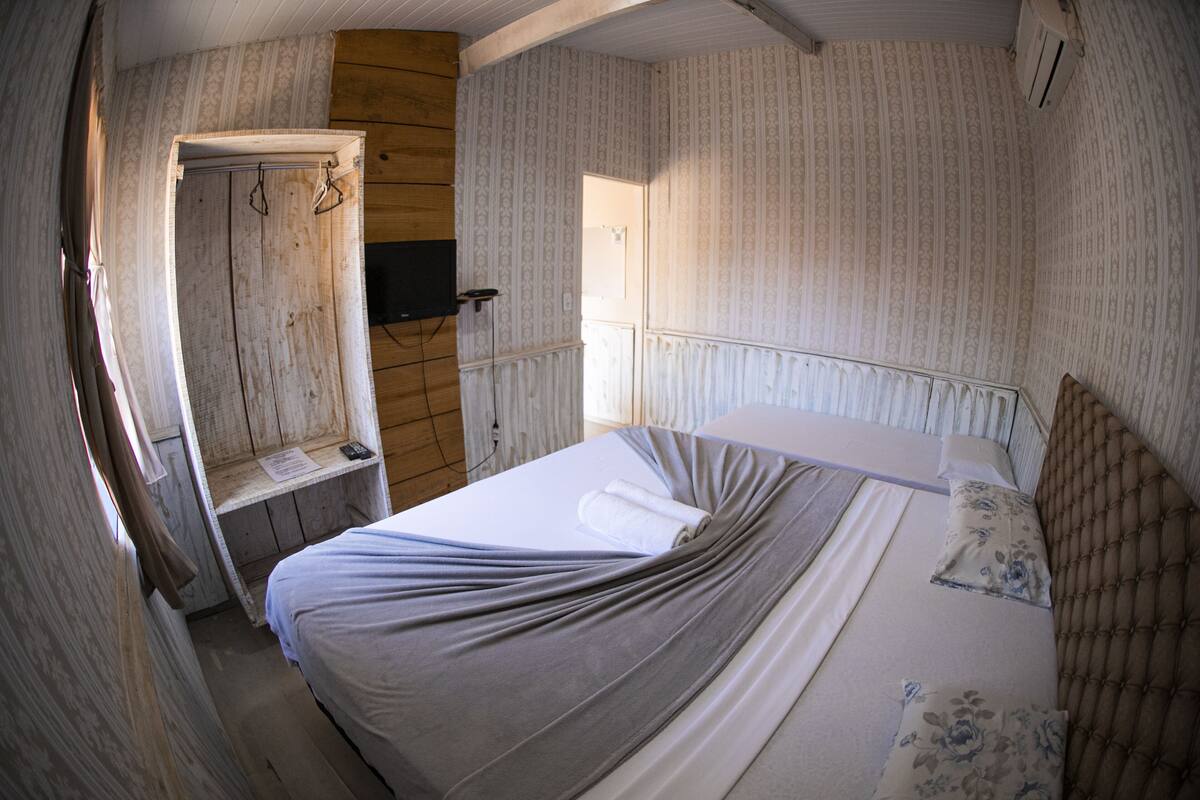 A bedroom with a bed, a wooden wardrobe, a television, and a door leading to another room.