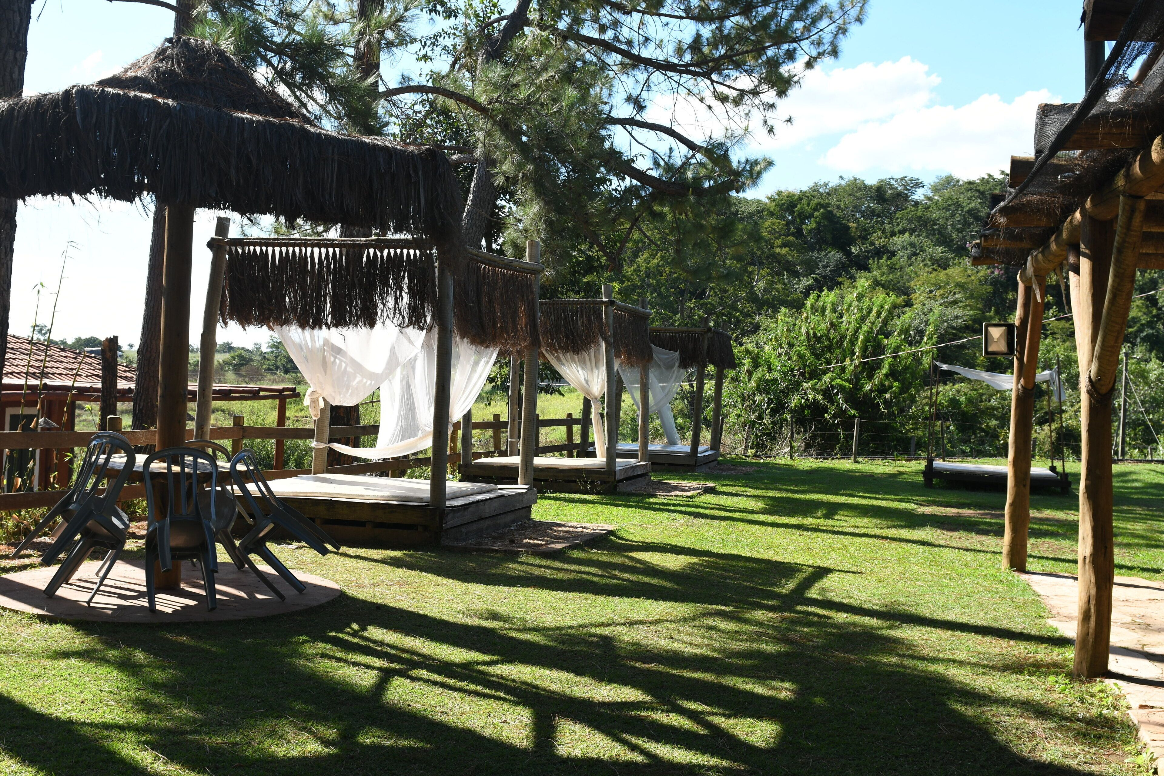Um gazebo com telhado de palha e cortinas brancas, cercado por um muro de madeira e cadeiras.